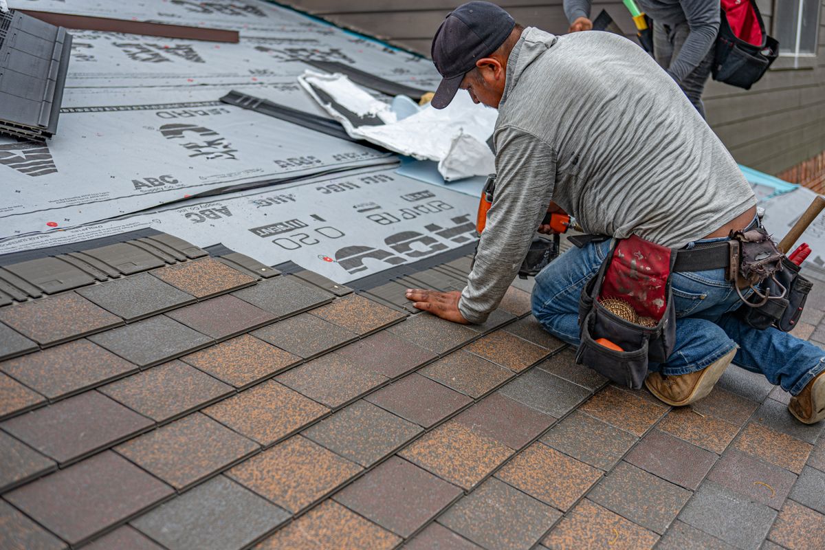 Roofer laying architectural asphalt shingles by hand